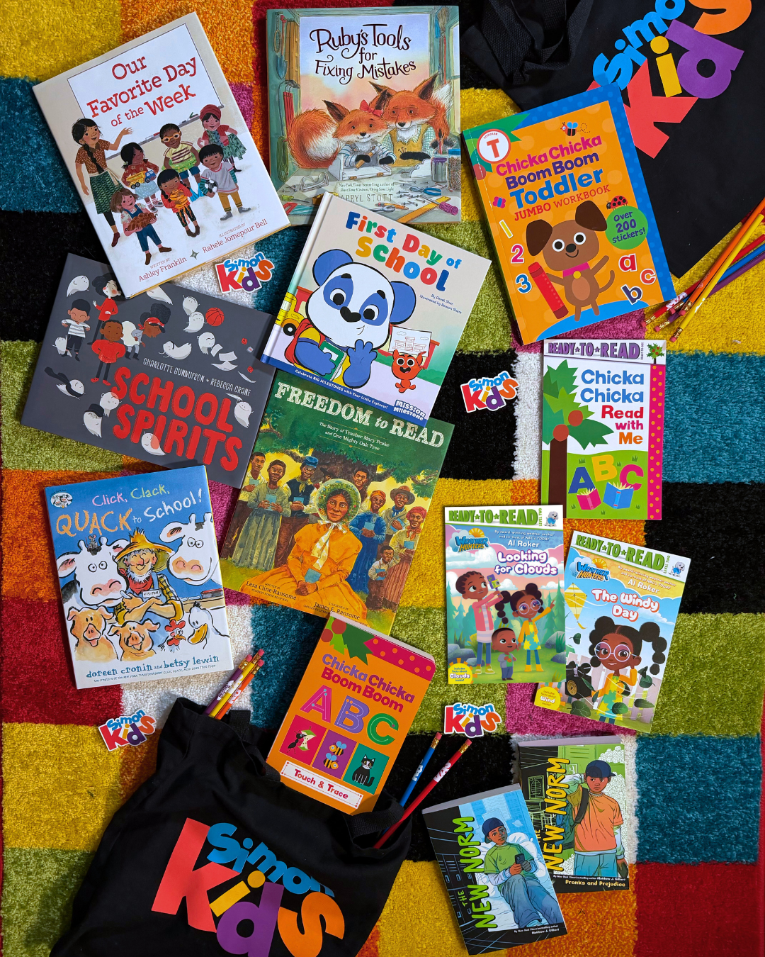 Several books with school themes on a multicolored carpet surrounded by Simon Kids branded pencils, stickers, and tote bags